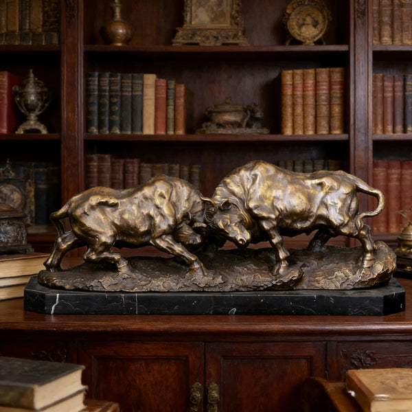 Bronze sculpture of two bulls on a marble base in front of a bookshelf.