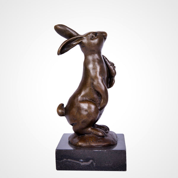This is a bronze rabbit sculpture: squatting with a carrot in its paws, upright long ears and lively expression, on a black stone base. It’s a cute home decor piece.