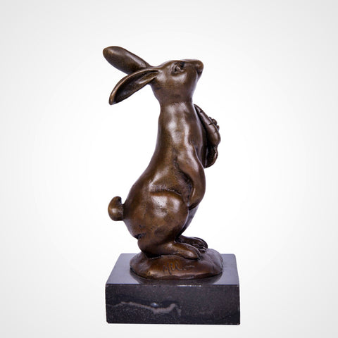This is a bronze rabbit sculpture: squatting with a carrot in its paws, upright long ears and lively expression, on a black stone base. It’s a cute home decor piece.